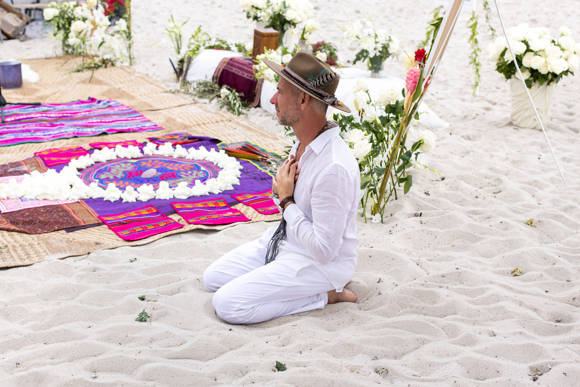 Tony Cho kneeling in ceremony beside a floral mandala on the beach