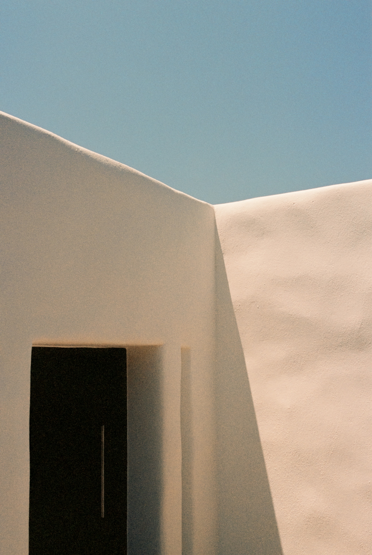 Sculptural white plaster architecture with a dark recessed doorway against a clear blue sky