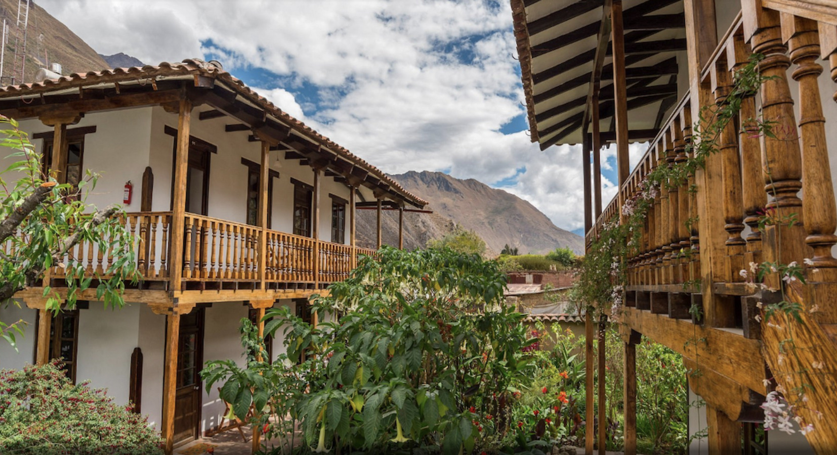 Wooden balcony courtyard at El Albergue Ollantaytambo with Sacred Valley mountains beyond