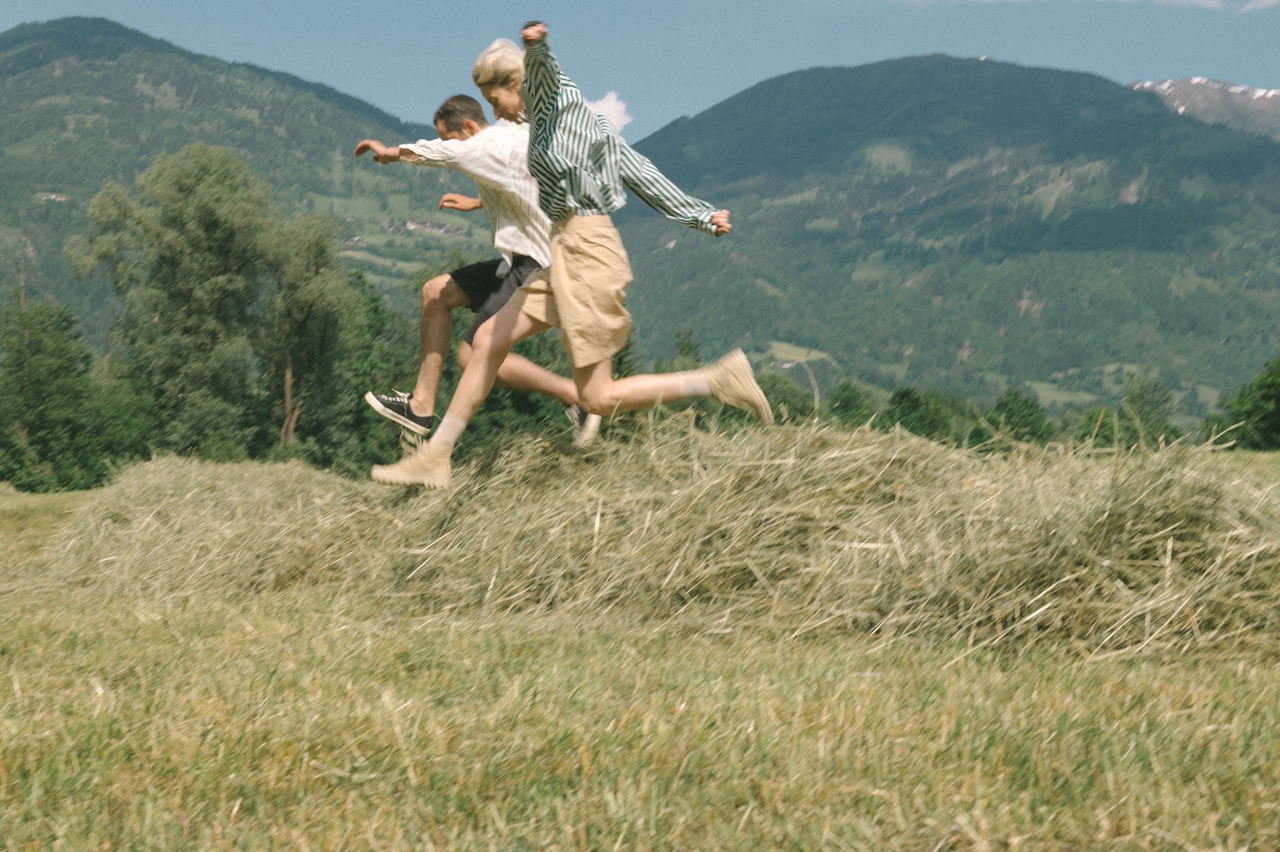 Two figures leaping across a hayfield in mountain light